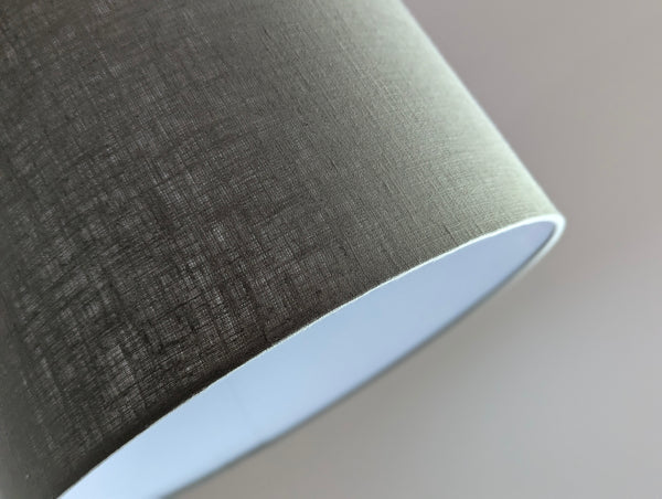 Close-up of an olive green lampshade with a linen textured fabric exterior and a white inner lining against a neutral background