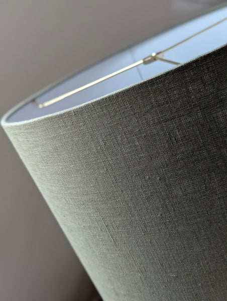 Close-up of an olive green lampshade with a linen textured fabric exterior and a white inner lining against a neutral background