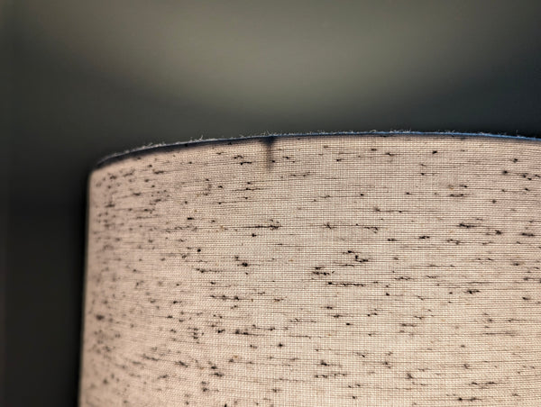 close up of a white lamp shade with small black flecks lit by a light bulb in a dark green room