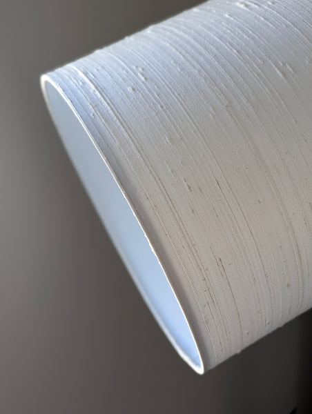 A close-up of a drum lampshade or drum light fixture with a textured, white silk, showing the inner surface and a dark background.