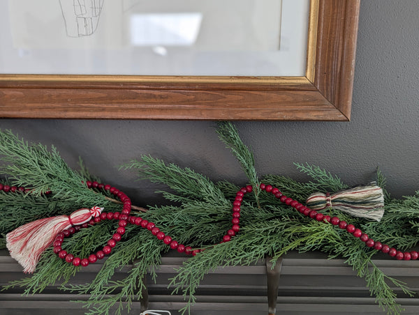 Decorative greenery with red garland and holiday tassels on a fireplace mantle