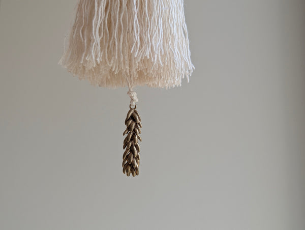 a small festive door tassel made of cotton with a green glass bead and brass accents