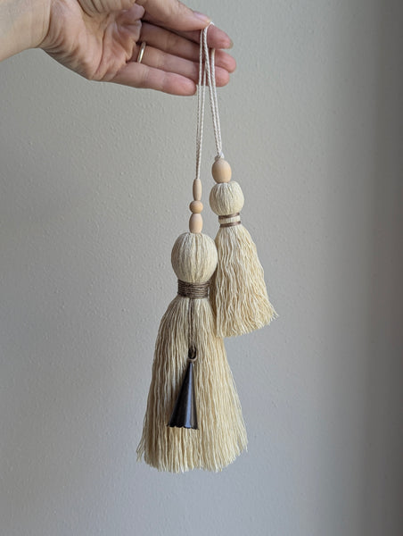 A close-up of a decorative tassel with cream-colored thread, a tan wrapped band, and a wooden beads shown against a neutral gray background