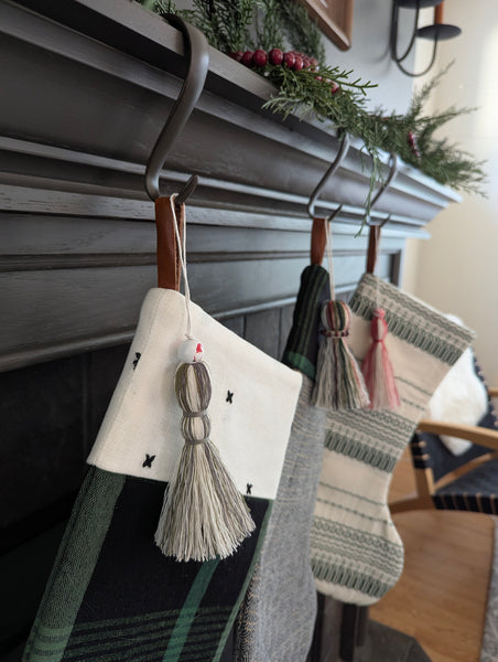 Three patterned stockings with tassel stocking charms hanging on a fireplace mantle.