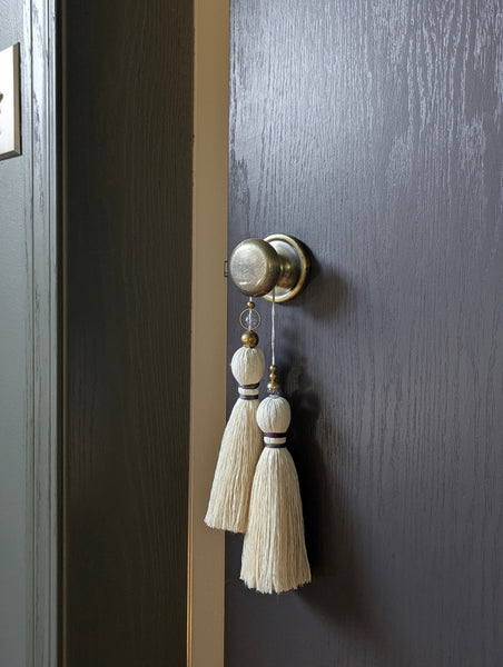 A close-up of a double tassel with deep purple colored thread, and glass and brass beads at the top dark door background