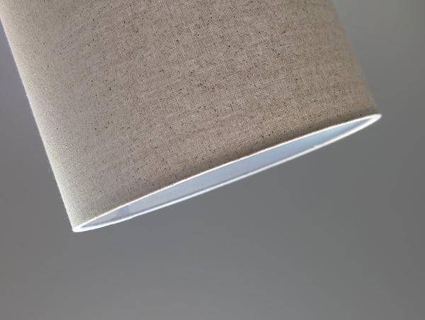 Speckled Oatmeal cotton fabric lampshade with brass hardware against a blurred background