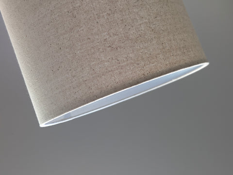 Speckled Oatmeal cotton fabric lampshade with brass hardware against a blurred background