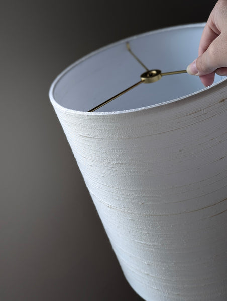 White silk lampshade with a hand holding it against a dark background