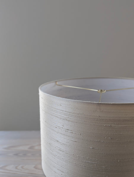 Close-up of a textured silk lampshade with brass hardware against a neutral background