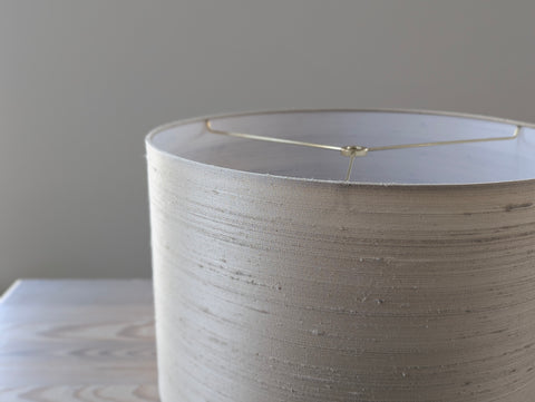 Close-up of a textured silk lampshade with brass hardware against a neutral background