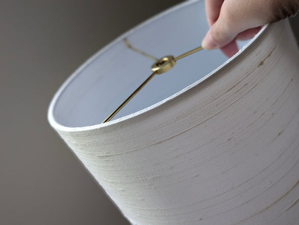 White silk lampshade with a hand holding it against a dark background