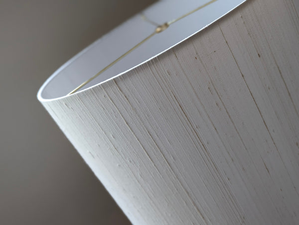 A close-up of a white silk lampshade with vertical grain