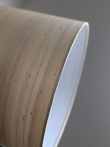 Close-up of a drum lamp shade with a silk texture and white interior on a gray background