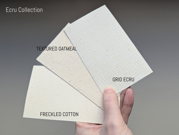 Three fabric lamp shade swatches labeled 'Textured Oatmeal', 'Grid Ecru', and 'Freckled Cotton' held by a hand against a gray background.