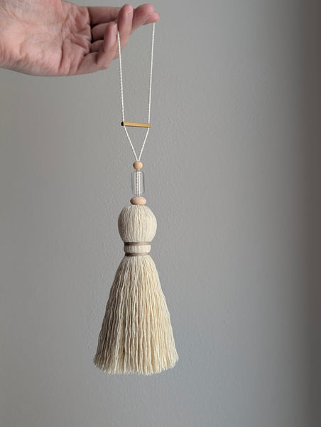 Decorative tassel with wooden and glass beads and a brass bar on a gray background
