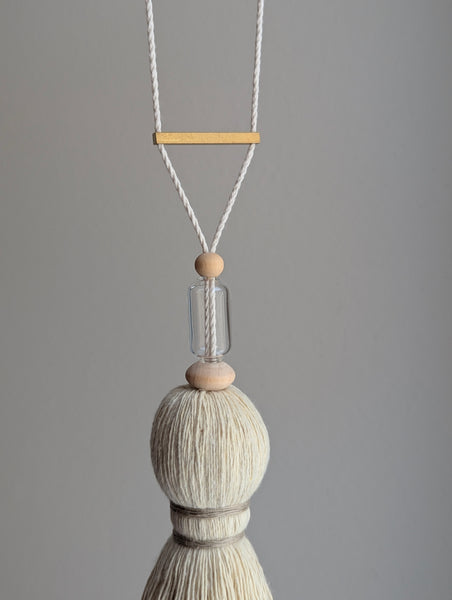 Decorative tassel with wooden and glass beads and a brass bar on a gray background