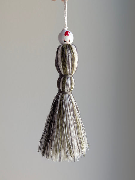 Holiday tassel ornament in green, white, and gray with a top bead featuring a red gnome with a long beard.