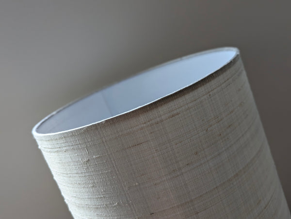 Close-up of a drum lampshade made of gray silk, showing the white inner lining and a neutral gray background.