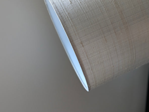 Close-up of a drum lampshade gray silk, showing the nubby texture and white inner lining against a neutral gray background.