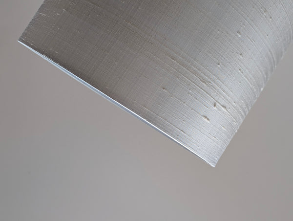 Close-up of a drum lampshade made of gray silk, showing the white inner lining and a neutral gray background.