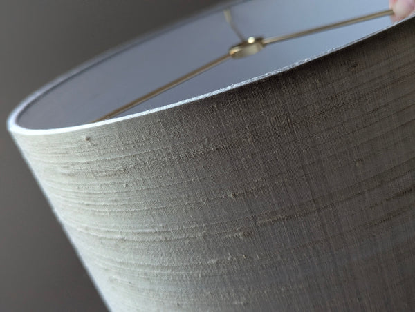 Close-up of a drum lampshade made of textured gray silk, showing the inner lining and brass hardware