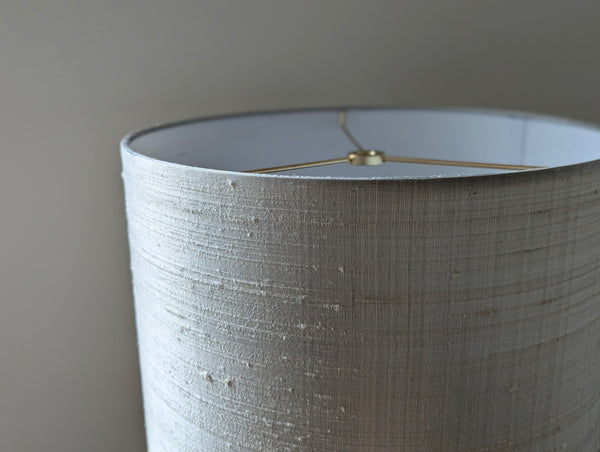Close-up of a drum lampshade with a textured, gray silk showing the interior and the brass spider hardware at the top.