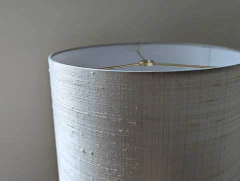 Close-up of a drum lampshade with a textured, gray silk showing the interior and the brass spider hardware at the top.