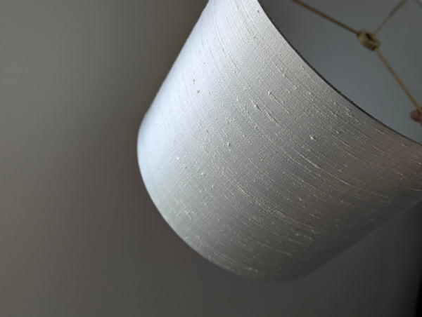A close-up of a drum lampshade made of textured gray silk, showing its nubby texture against a neutral gray background.