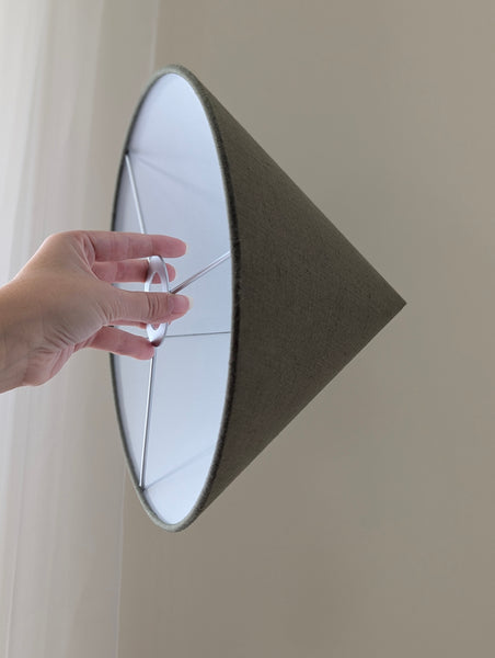 person's hand holding an olive green linen cone lamp shade with nickel hardware