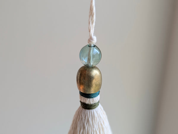 a small festive door tassel made of cotton with a green glass bead and brass accents