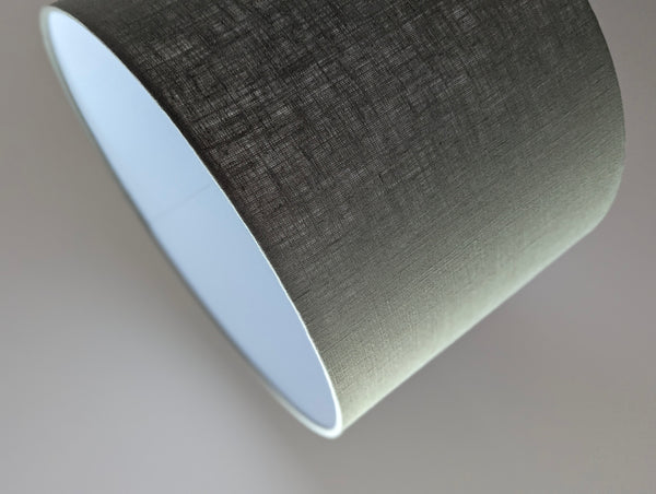 Close-up of an olive green lampshade with a linen textured fabric exterior and a white inner lining against a neutral background