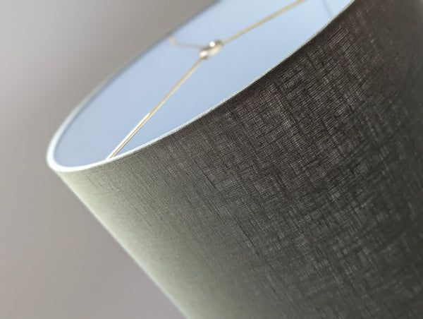 Close-up of an olive green lampshade with a linen textured fabric exterior and a white inner lining against a neutral background