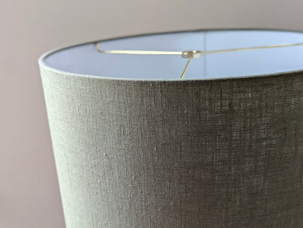 Close-up of an olive green lampshade with a linen textured fabric exterior and a white inner lining against a neutral background