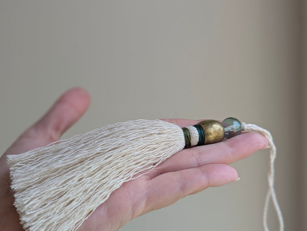 a small festive door tassel made of cotton with a green glass bead and brass accents