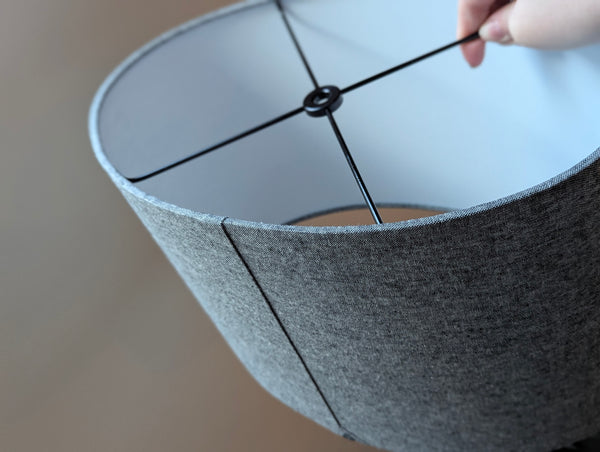 back side of an oval-shaped, flat-sided lamp shade in dark grey fabric with black hardware