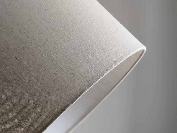 Speckled Oatmeal cotton fabric lampshade with brass hardware against a blurred background