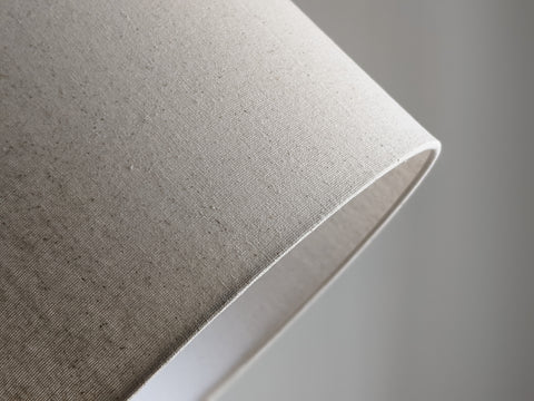 Speckled Oatmeal cotton fabric lampshade with brass hardware against a blurred background