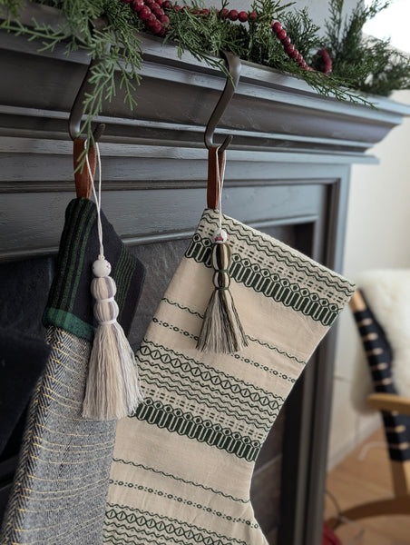 Two patterned stockings with tassels hanging on a fireplace mantle.