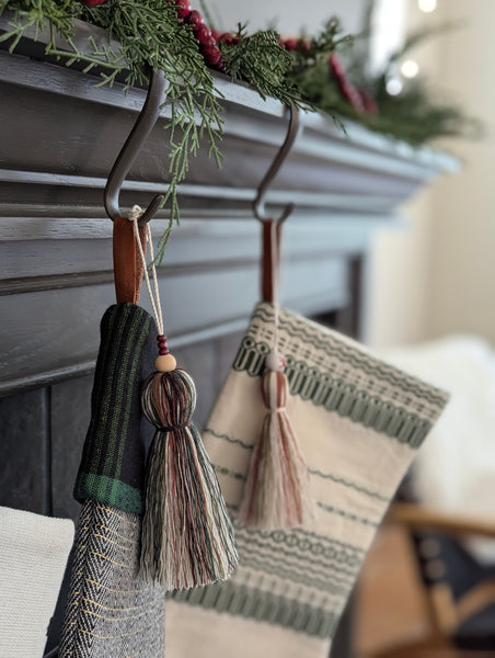 two stockings hanging on a fireplace mantle with holiday tassel charms