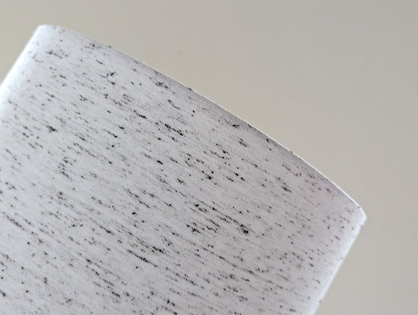 close up of a white lamp shade with small black flecks throughout the fabric 