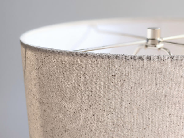 Speckled Oatmeal cotton fabric lampshade with brass hardware against a blurred background
