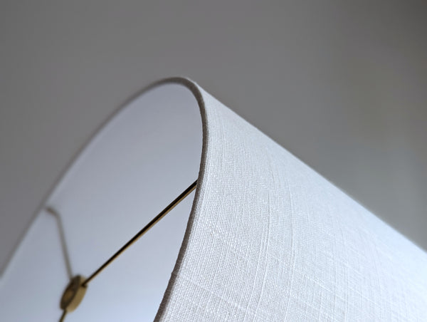 Close-up of a white linen lampshade with brass spider washer hardware against a neutral background