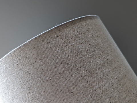 Speckled Oatmeal cotton fabric lampshade with brass hardware against a blurred background