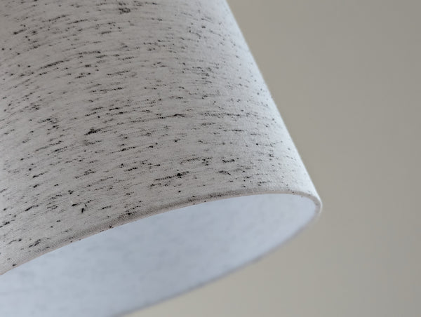 close up of a white lamp shade with small black flecks throughout the fabric resembling an oreo blizzard
