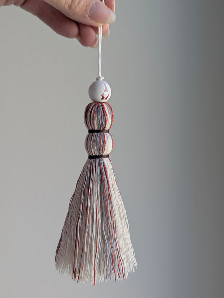 Christmas tassel with wooden gnome bead in red and white held by a hand against a gray background