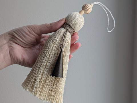 Hand holding a decorative tassel against a plain background
