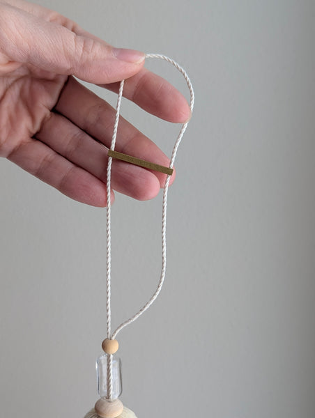Decorative tassel with wooden and glass beads and a brass bar on a gray background