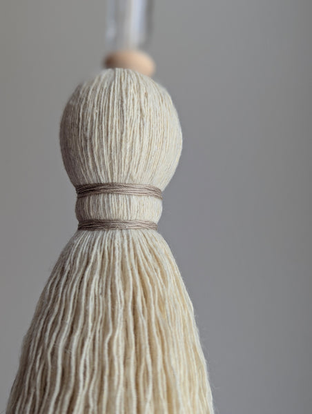 Decorative tassel with wooden and glass beads and a brass bar on a gray background