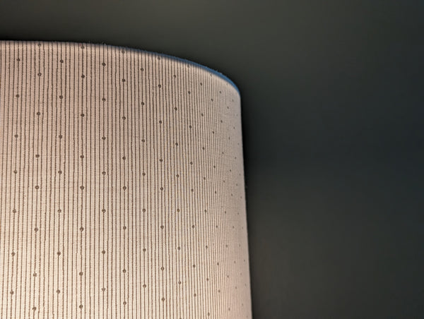close up of white lamp shade with polka dots and stripes, lit in a dark green room