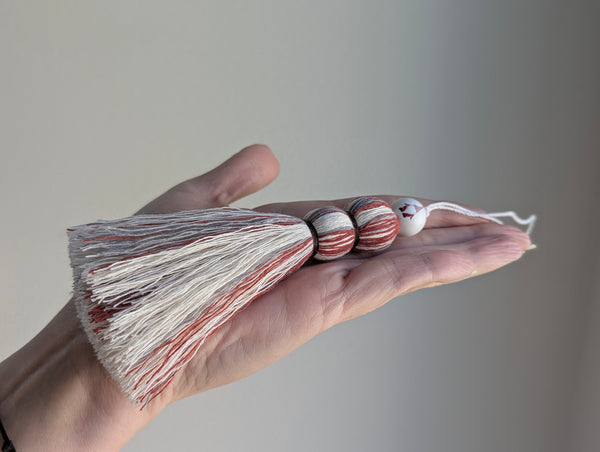 Hand holding a cotton tassel in red, white, and gray with a seasonal gnome design